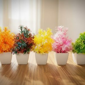 Colorful mini plant pots with artificial plants in small white containers arranged on a table for home and office decoration.